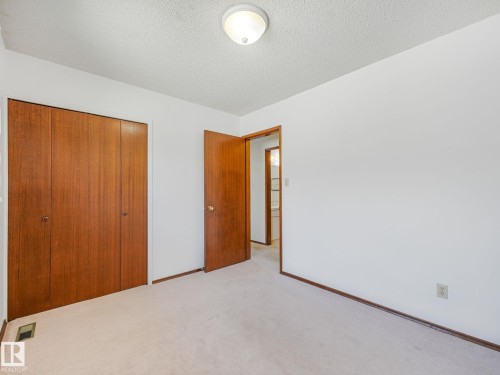Bedroom featuring neutral carpet flooring, white walls, wood-paneled bi-fold closet doors, and a ceiling-mounted light fixture - 15011 72A Street, Edmonton, AB 