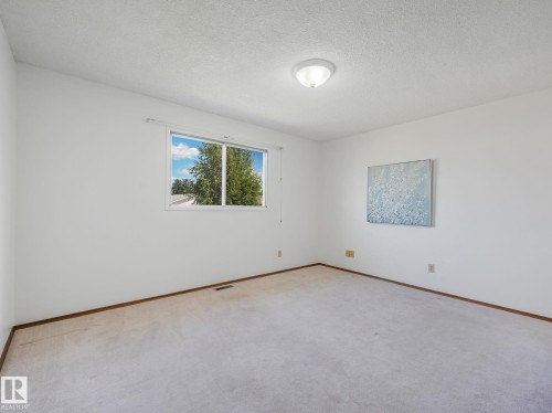 Spacious interior room featuring a large window, neutral wall paint, and overhead lighting - 15011 72A Street, Edmonton, AB 