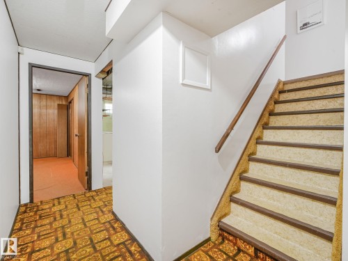 Staircase featuring a wood handrail and carpeted treads, alongside a hallway with patterned flooring - 15011 72A Street, Edmonton, AB 