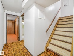 Staircase featuring a wood handrail and carpeted treads, alongside a hallway with patterned flooring - 