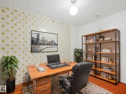 Dedicated office space featuring patterned wallpaper, wood-finish flooring, a built-in shelving unit, and overhead lighting - 