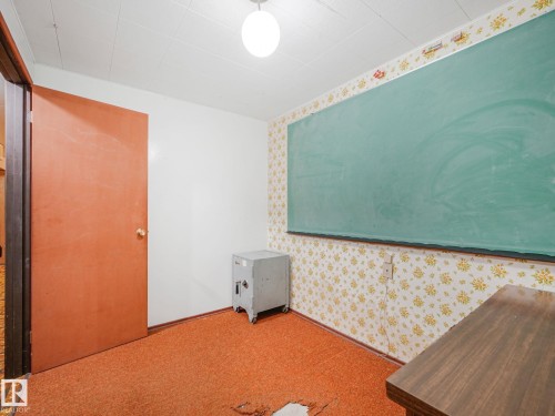 Interior room featuring a large green chalkboard, patterned wallpaper, orange carpeting, a solid core door, and an overhead light fixture - 15011 72A Street, Edmonton, AB 