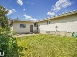 Expansive grassy yard area with a stucco exterior, concrete foundation accents, and multiple windows - 