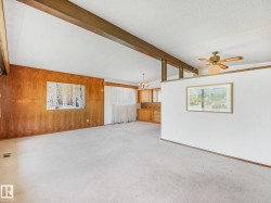 Spacious room featuring a vaulted ceiling with exposed wood beams, a wood-paneled accent wall, and light-toned carpeting - 