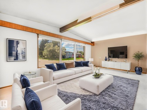 Vaulted ceiling with exposed wood beams, expansive windows, wood-finish flooring, and a neutral color palette create a bright, open living space - 15011 72A Street, Edmonton, AB 