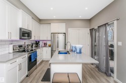 Modern kitchen featuring white cabinetry, stainless steel appliances, a large center island with an undermount sink, light gray countertops, and wood-finish flooring - 
