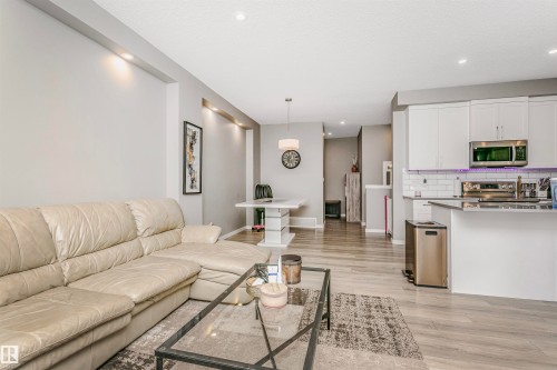 Open-concept living space featuring wood-finish flooring, recessed lighting, and a kitchen with white cabinetry, subway tile backsplash, and stainless steel appliances - 7322 Chivers Crescent, Edmonton, AB 