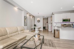 Open-concept living space featuring wood-finish flooring, recessed lighting, and a kitchen with white cabinetry, subway tile backsplash, and stainless steel appliances - 