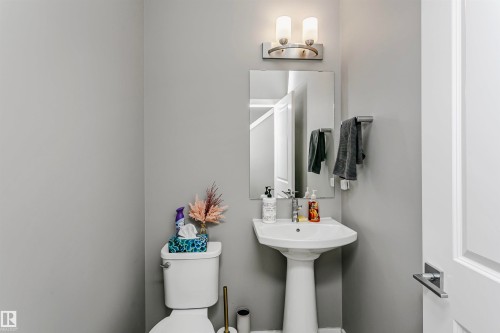 Pedestal sink with a wall-mounted mirror, brushed nickel vanity lighting, and a coordinating towel bar - 7322 Chivers Crescent, Edmonton, AB 