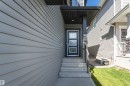 Contemporary entryway featuring a dark blue door with three horizontal glass panels, concrete steps, and a black metal handrail - 7322 Chivers Crescent, Edmonton, AB 