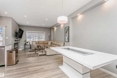 Open-concept living space featuring wood-finish flooring, recessed lighting, and a white kitchen island with integrated lighting - 7322 Chivers Crescent, Edmonton, AB 