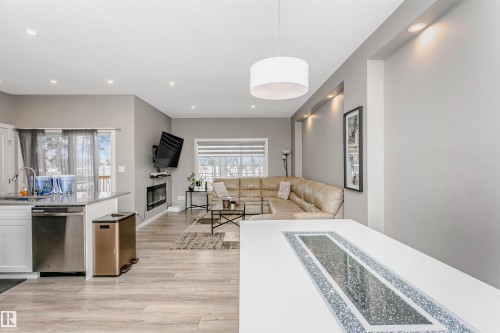 Open-concept living area featuring wood-finish flooring, a kitchen island with a stone-finish countertop, a built-in fireplace, recessed lighting, and a modern drum pendant light fixture - 7322 Chivers Crescent, Edmonton, AB 