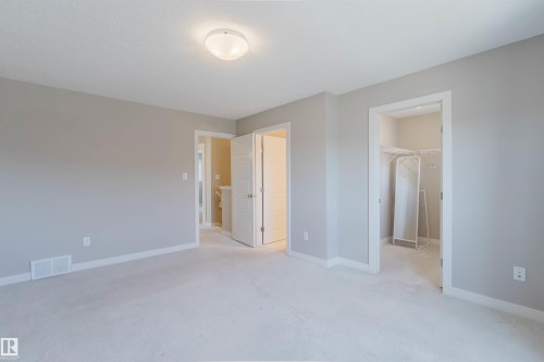 Spacious room featuring light gray wall paint, white trim, light-colored carpeting, a flush-mount ceiling light fixture, and an open doorway revealing a closet with wire shelving - 2472 Glenridding Boulevard, Edmonton, AB 