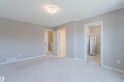 Spacious room featuring light gray wall paint, white trim, light-colored carpeting, a flush-mount ceiling light fixture, and an open doorway revealing a closet with wire shelving - 