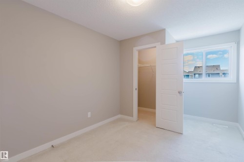 Neutral-toned interior room featuring light carpet flooring, a walk-in closet with built-in shelving, and a window with white trim - 2472 Glenridding Boulevard, Edmonton, AB 