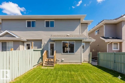 Expansive grassy yard area featuring light green fencing and a multi-level wood deck leading to a glass-paneled door - 2472 Glenridding Boulevard, Edmonton, AB 