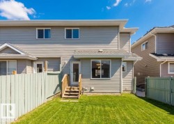 Expansive grassy yard area featuring light green fencing and a multi-level wood deck leading to a glass-paneled door - 