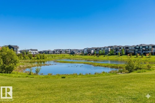 Manicured green spaces surrounding a tranquil pond, bordered by contemporary residential structures - 2472 Glenridding Boulevard, Edmonton, AB 