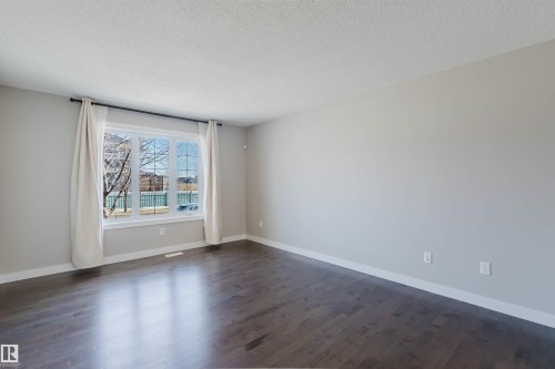 Spacious room featuring wood-finish flooring, a large window, light gray wall paint, and white trim - 2472 Glenridding Boulevard, Edmonton, AB 