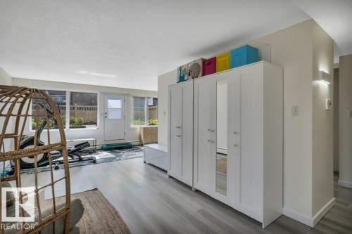 Sunlit room featuring wood-finish flooring, a full wall of windows, and a white paneled door - 102 7805 159 Street, Edmonton, AB 