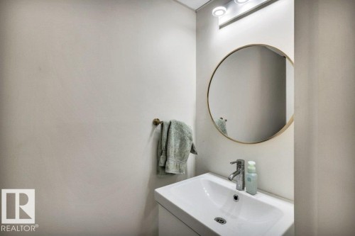 Bathroom featuring a wall-mounted vanity with an integrated sink, polished chrome faucet, round framed mirror, and overhead track lighting - 102 7805 159 Street, Edmonton, AB 