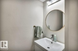Bathroom featuring a wall-mounted vanity with an integrated sink, polished chrome faucet, round framed mirror, and overhead track lighting - 