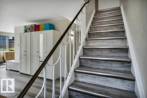 Staircase featuring wood-finish treads with metallic risers, white balusters, and a dark handrail - 102 7805 159 Street, Edmonton, AB 