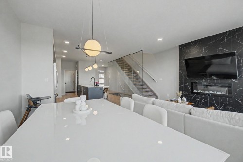 Open-concept living space featuring a black marble-look accent wall with an inset fireplace, glass panel stair railing, and contemporary pendant lighting fixtures - 3313 Kulay Way, Edmonton, AB 