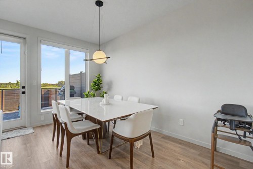 Dining area featuring a modern linear chandelier, wood-finish flooring, and expansive windows - 3313 Kulay Way, Edmonton, AB 