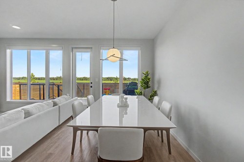 Open-concept living area featuring wood-finish flooring, a contemporary pendant light fixture, and a large dining table - 3313 Kulay Way, Edmonton, AB 
