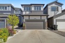 Contemporary home exterior featuring a dark gray garage door, stone accents, horizontal siding, and a paved driveway - 3313 Kulay Way, Edmonton, AB 