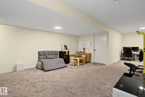Spacious carpeted room featuring recessed lighting, light neutral wall tones, and a white door with a black hardware - 3313 Kulay Way, Edmonton, AB 