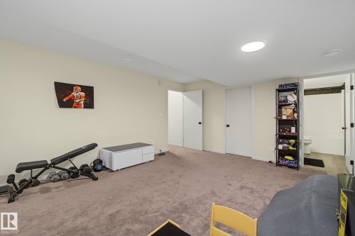 Spacious carpeted room featuring a ceiling light fixture, white walls, and a pair of white doors with black hardware - 3313 Kulay Way, Edmonton, AB 