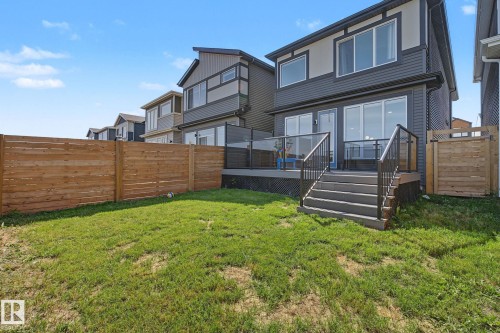 Rear exterior featuring a spacious deck with glass panel railing, sliding patio doors, and exterior stairs to the yard - 3313 Kulay Way, Edmonton, AB 