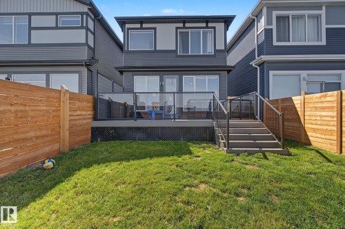 Rear exterior featuring a multi-level deck with glass panel railings, dark wood-tone stairs, sliding glass patio doors, and a manicured lawn - 3313 Kulay Way, Edmonton, AB 