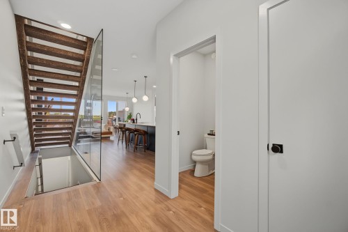 Open-concept living space featuring wood-finish flooring, a contemporary staircase with glass railing, and a powder room with a commode - 3313 Kulay Way, Edmonton, AB 