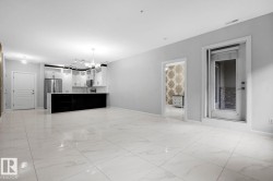 Open-concept living area featuring large format tile flooring and a kitchen with white cabinetry, stainless steel appliances, and a dark island - 
