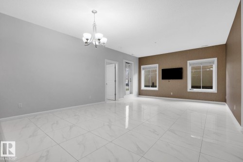 Spacious room featuring large format tile flooring, a contemporary chandelier, multiple windows, and a neutral color palette - 105 160 Magrath Road, Edmonton, AB 