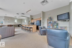 Spacious common area featuring textured carpeting, a kitchen area with light wood cabinetry, and a peninsula with bar seating - 