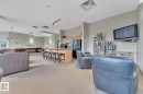 Spacious common area featuring textured carpeting, a kitchen area with light wood cabinetry, and a peninsula with bar seating - 105 160 Magrath Road, Edmonton, AB 