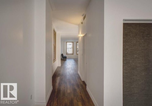 Hallway featuring wood-finish flooring, white baseboards, and crown molding - 210 10134 100 Street, Edmonton, AB 