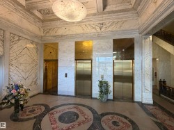 Grand lobby featuring three brass-toned elevators and white marble wall paneling - 