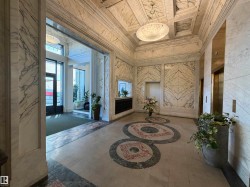 Grand lobby featuring extensive marble wall cladding with intricate veining, a coffered ceiling, and a large circular flush-mount light fixture - 