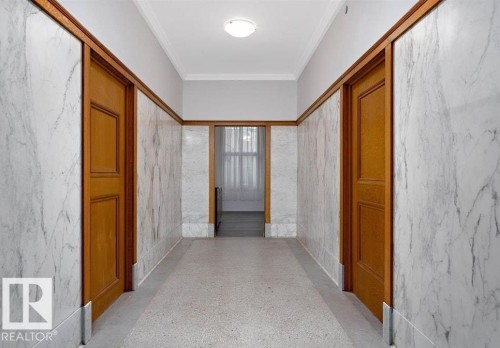 Hallway featuring marble-clad walls, wood door casings, wood-finish baseboards, and terrazzo flooring - 210 10134 100 Street, Edmonton, AB 