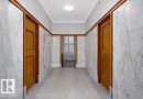 Hallway featuring marble-clad walls, wood door casings, wood-finish baseboards, and terrazzo flooring - 210 10134 100 Street, Edmonton, AB 