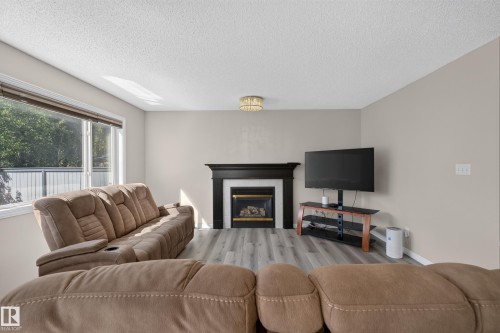 Living area featuring a fireplace with a black mantel, light gray walls, wood-finish flooring, a contemporary ceiling light fixture, and a large window - 2327 37B Avenue, Edmonton, AB 