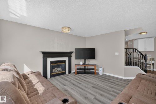 Living area featuring a black fireplace with a white surround, wood-finish flooring, and light neutral wall paint - 2327 37B Avenue, Edmonton, AB 