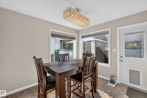 Dining area featuring a contemporary rectangular chandelier, tile flooring, and multiple windows providing natural light - 2327 37B Avenue, Edmonton, AB 