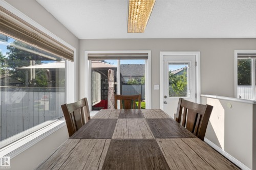 Dining area with wood-finish flooring, featuring a large window with a roller shade, a sliding glass door, an exterior door with integrated blinds, and an overhead decorative light fixture - 2327 37B Avenue, Edmonton, AB 