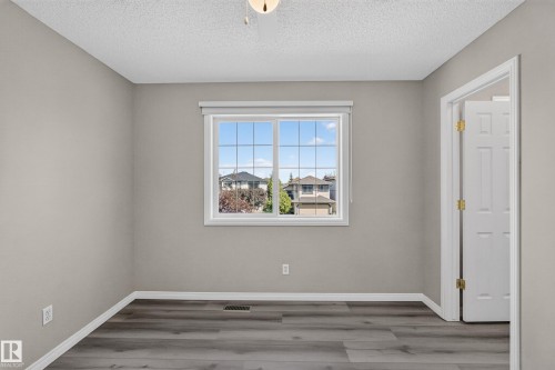 Spacious room featuring wood-finish flooring, a white trim window, neutral wall paint, and a white paneled door with brass hardware - 2327 37B Avenue, Edmonton, AB 